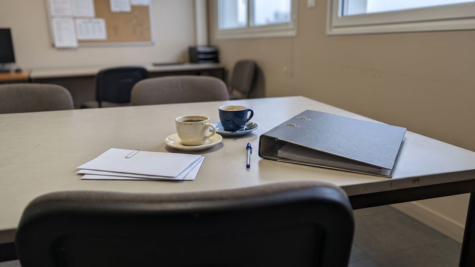 Classeur fermé et pile d'enveloppes sur une table de salle de pause, lumière grise du matin