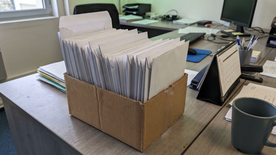 Boîte en carton remplie d'enveloppes blanches identiques sur un bureau gris de CSE